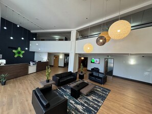 A spacious lobby with a reception desk, black sofas, a coffee table, and hanging pendant lights.