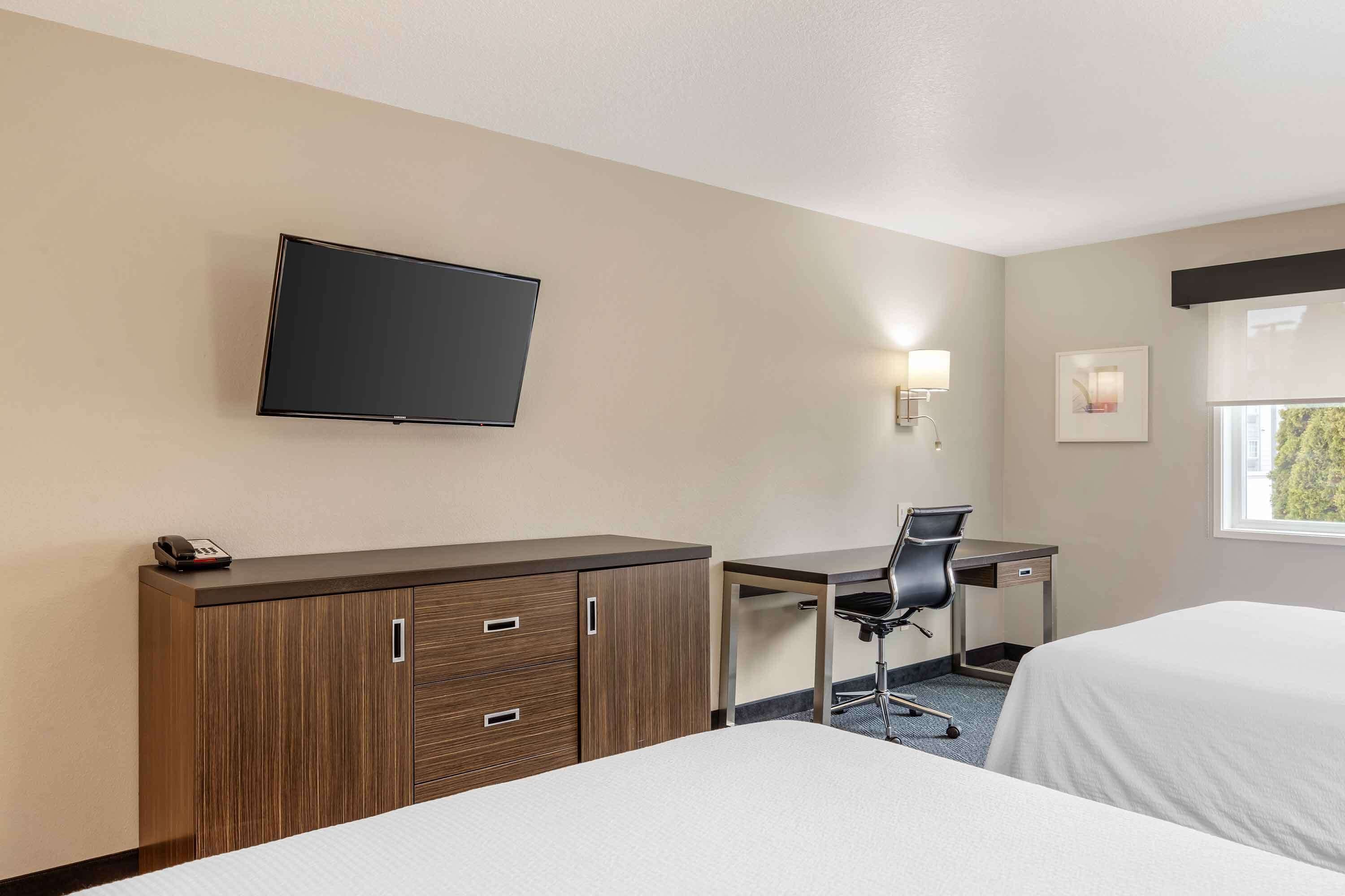 Ein Hotelzimmer mit zwei Betten, einem Schreibtisch mit Stuhl, einem an der Wand montierten Fernseher und einem kleinen Fenster.