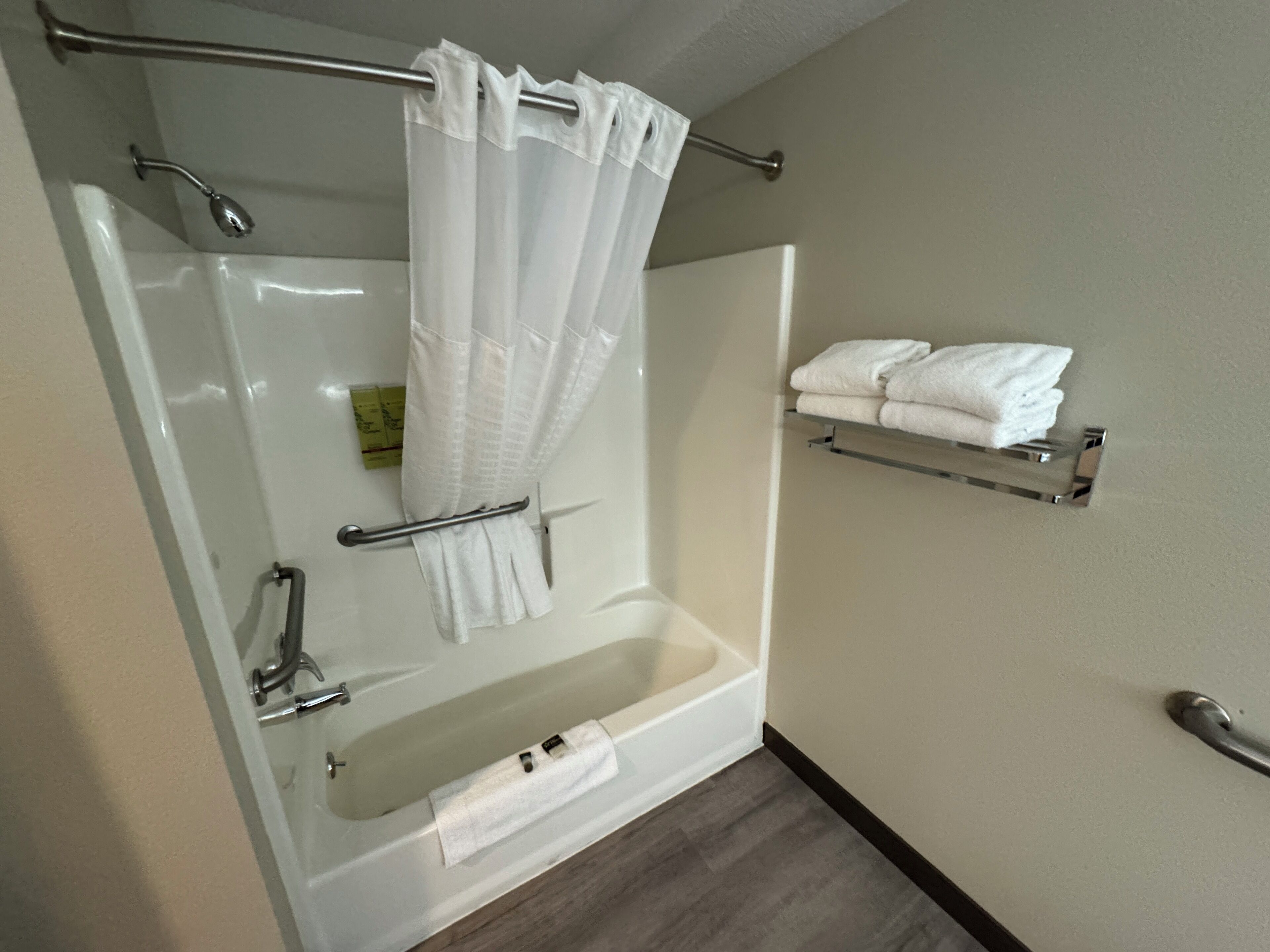 A modern bathroom with a bathtub, a shower, a handrail, and a towel rack.