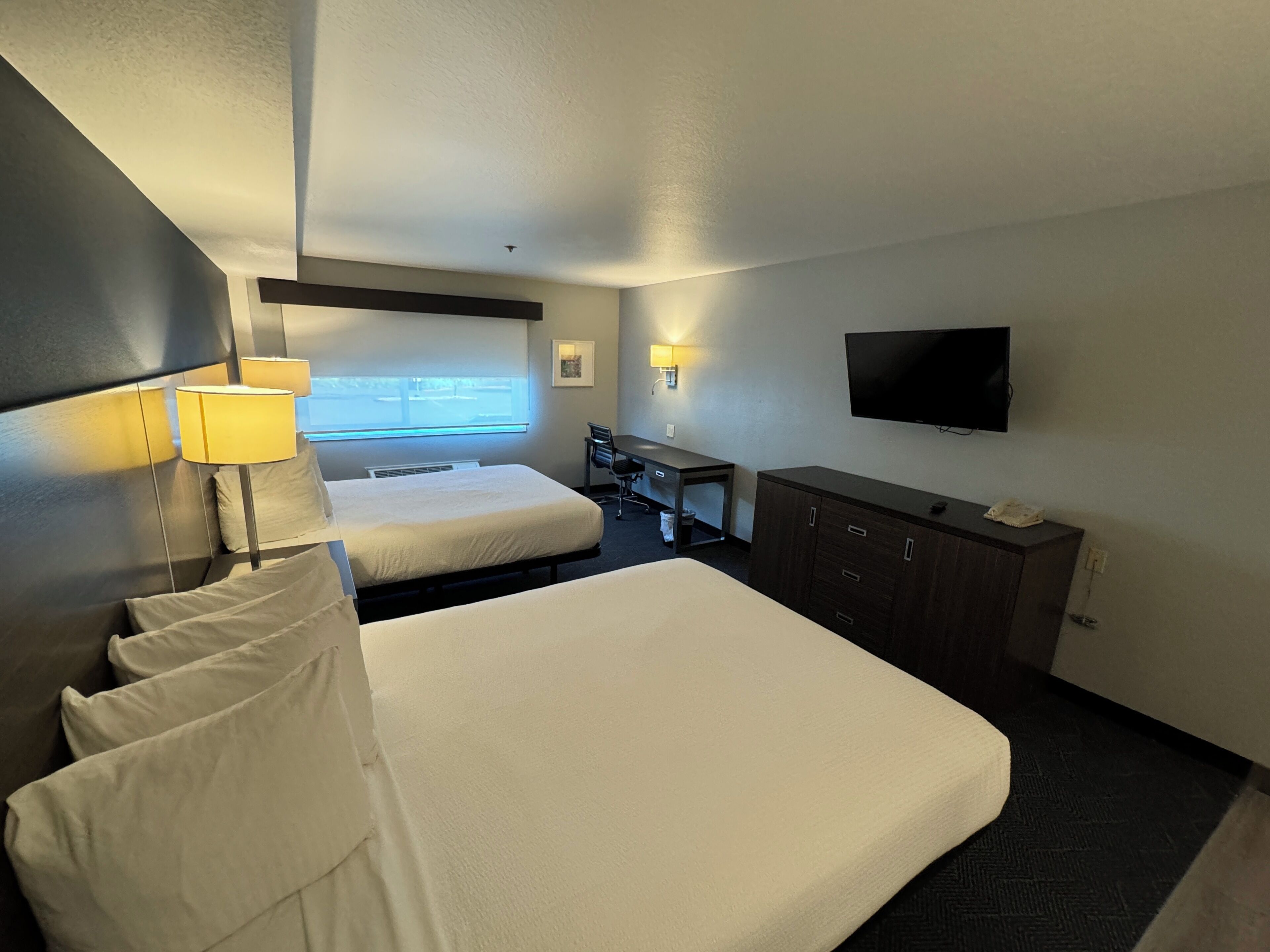 A hotel room with a large bed, a desk, a chair, a TV, and a window with a view.