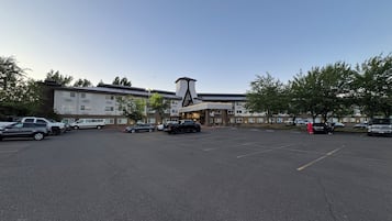 Ein Parkplatz mit mehreren Autos, ein Gebäude im modernen Stil und Bäume.