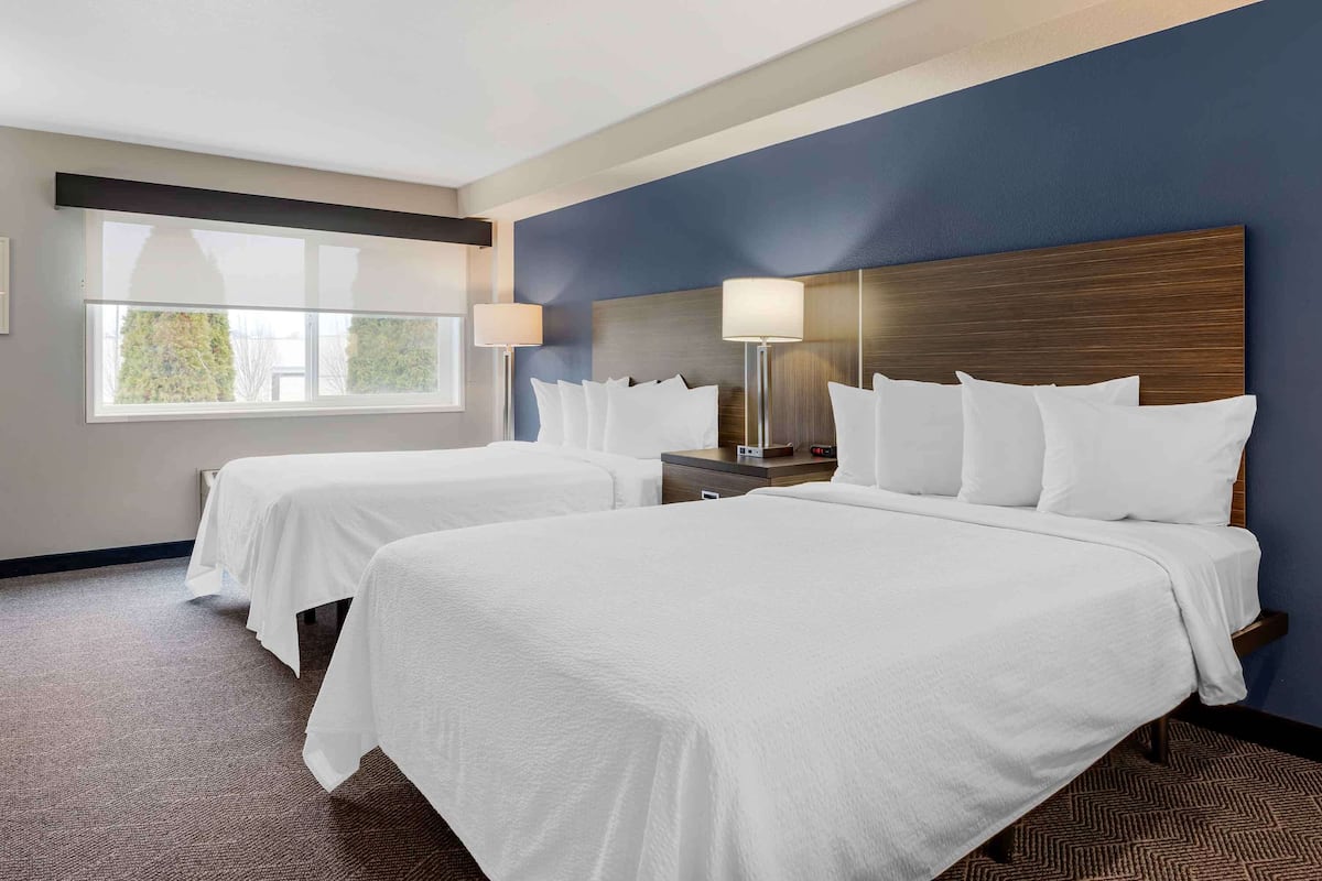 Une chambre d’hôtel avec deux lits, une grande fenêtre et une table de chevet avec une lampe.