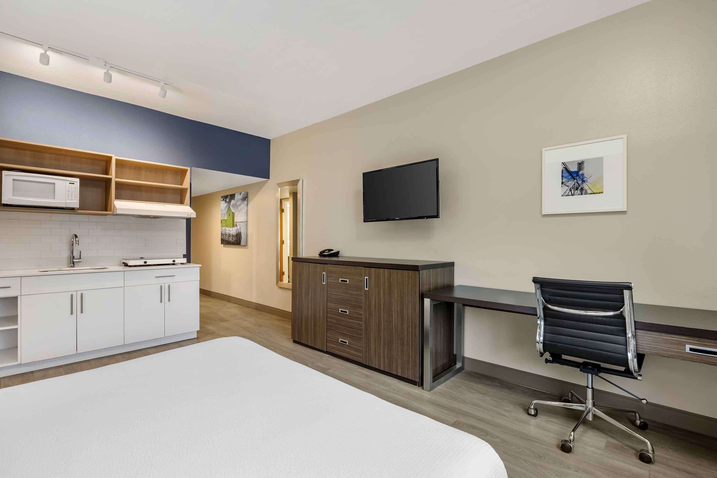 Una habitación de hotel moderna con cama, escritorio, televisor de pantalla plana y kitchenette.