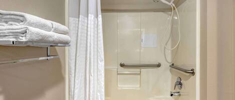 A walk-in shower with a glass door, a towel rack with folded towels, and a handrail.