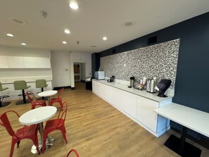 A modern kitchen with white cabinets, a patterned backsplash, and a wooden floor. There are red chairs and a white table.