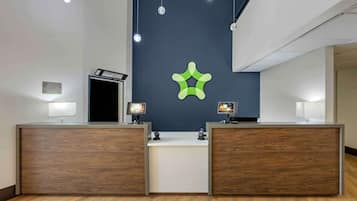 A reception desk with a dark wall and a green logo, two monitors, and a wooden floor.