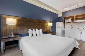 A hotel room with a large bed, bedside lamps, a wooden headboard, a desk with a lamp, a microwave, and a small kitchenette.