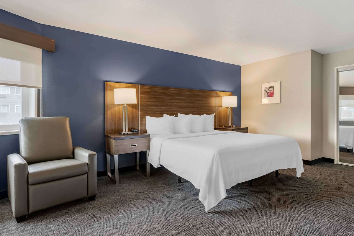 Une chambre d’hôtel avec un lit, une chaise, une table de chevet et une lampe.