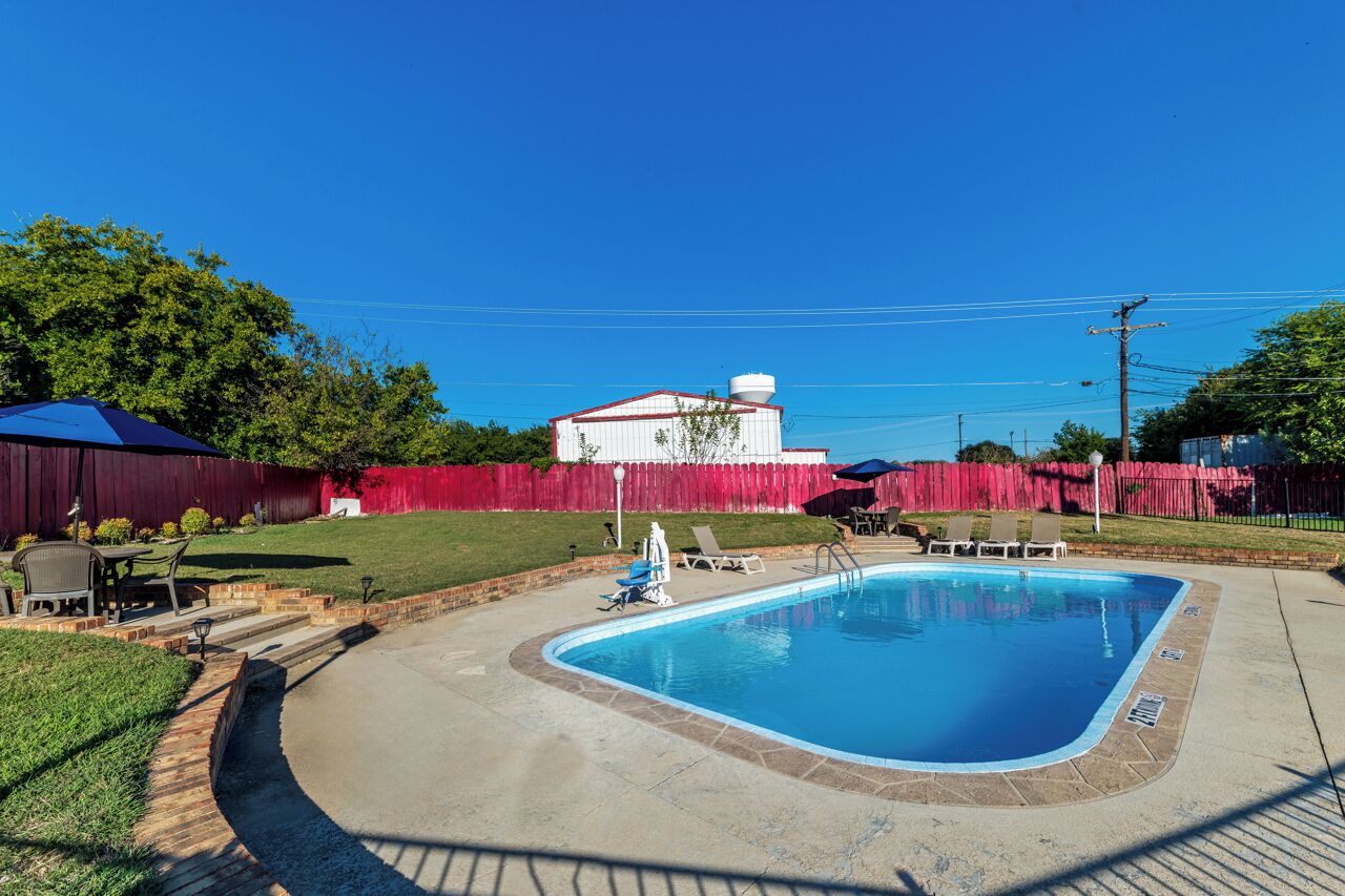Una piscina con valla roja, un edificio blanco y cielo azul despejado.
