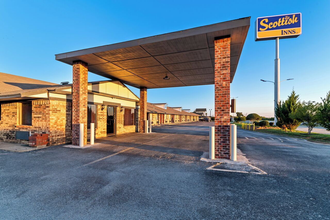 A Scottish Inn with a covered parking area, brick buildings, and a clear sky.