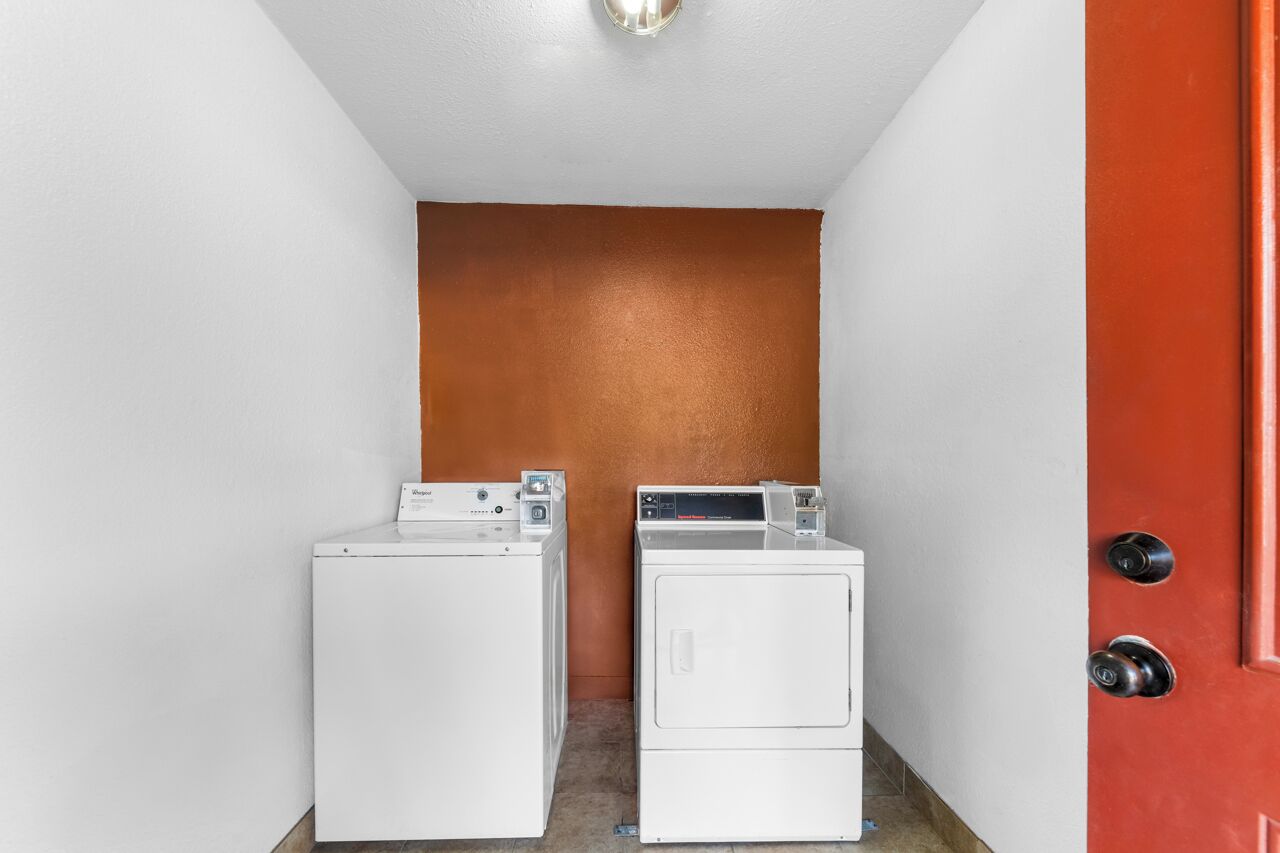 Uma lavanderia com duas máquinas de lavar brancas e uma porta vermelha.