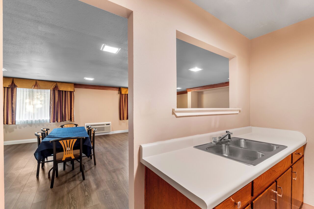 A room with a dining table and chairs, a kitchen area with a sink and cabinets, and a ceiling with recessed lighting.