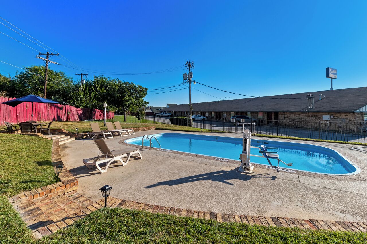 A swimming pool with lounge chairs, a diving board, and a brick patio area.