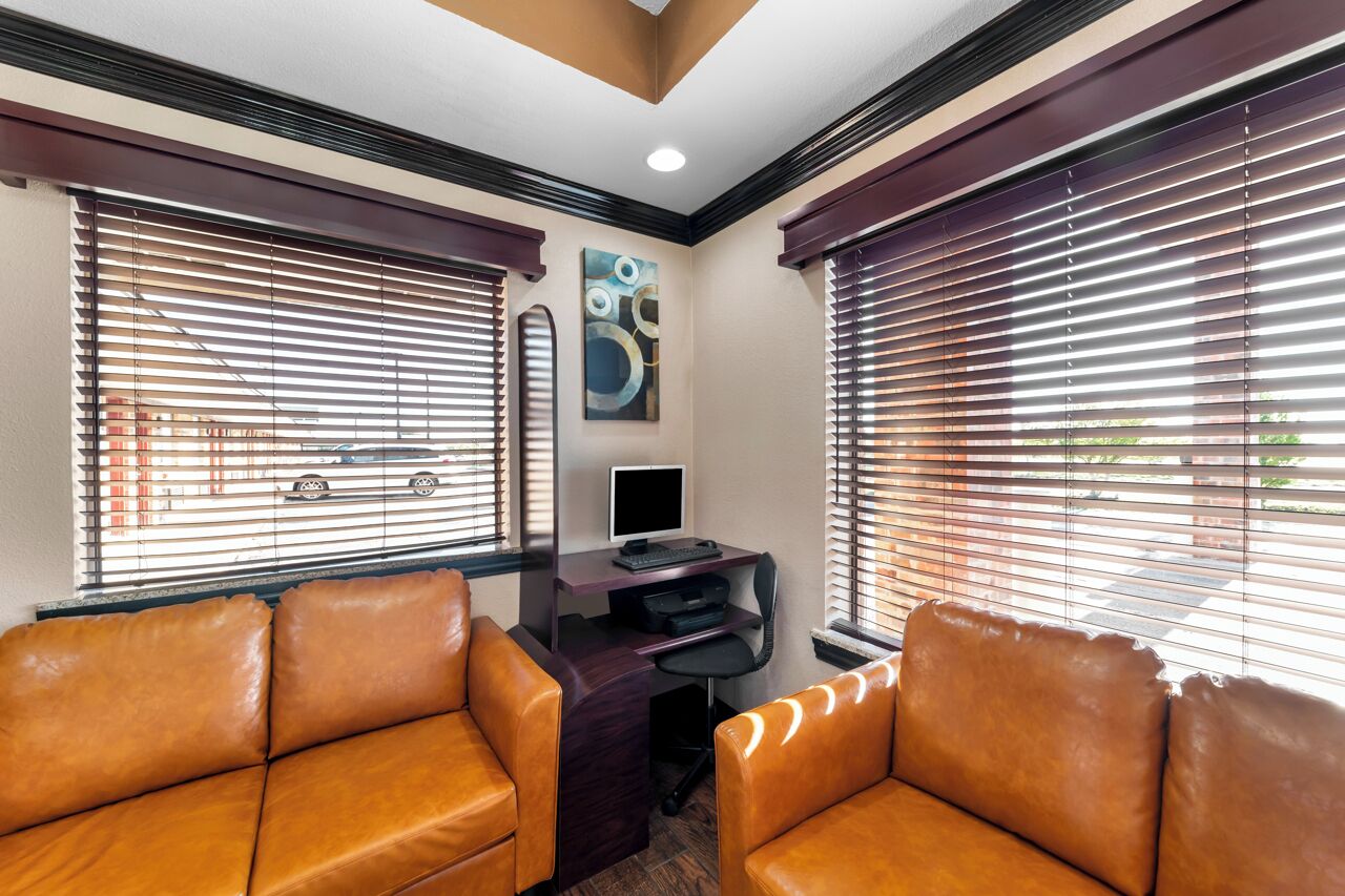 A room with two leather sofas, a desk with a computer, and large windows with blinds.