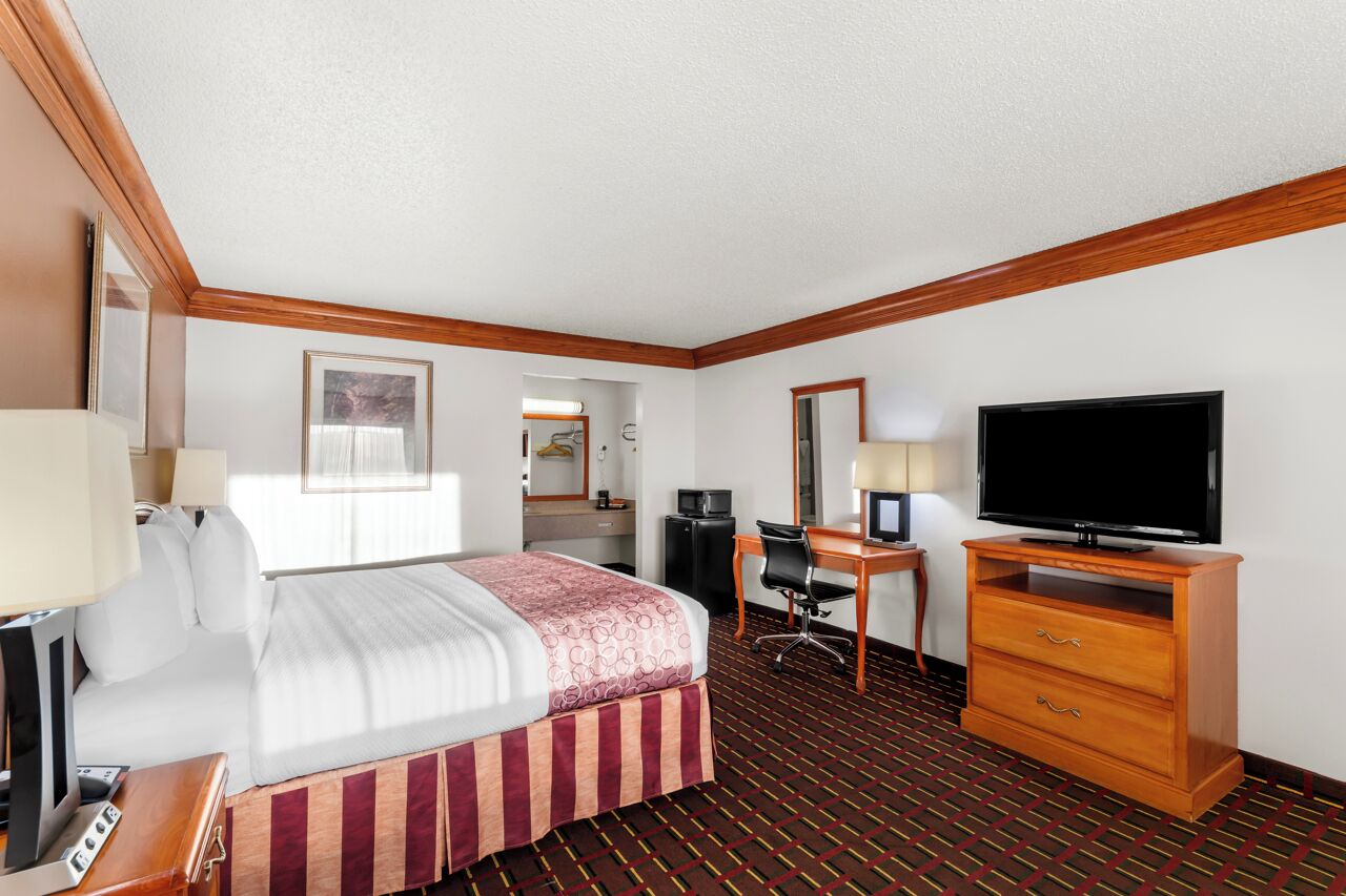 A hotel room with a bed, desk, television, and a mirror.
