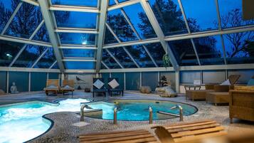 An indoor swimming pool with wooden loungers and a glass ceiling.