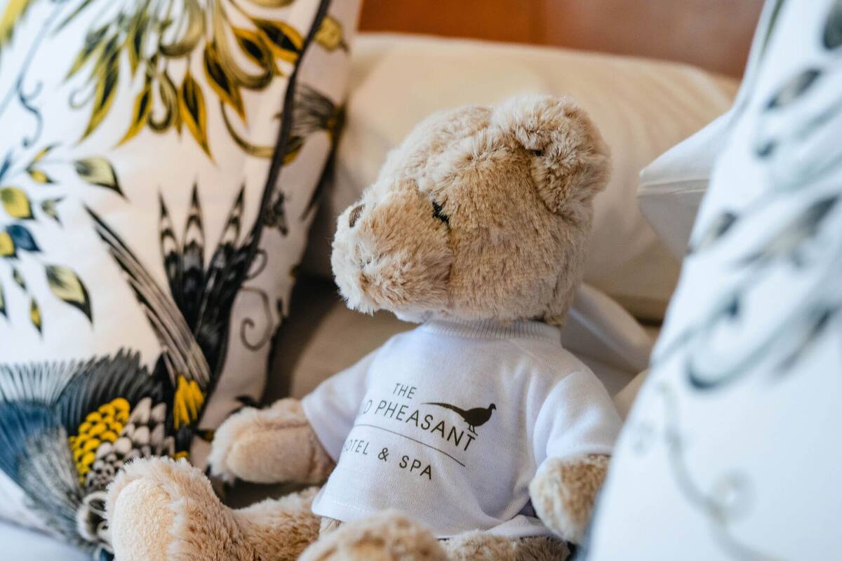 Un peluche con camisa, colocado sobre una cama con almohadones estampados.
