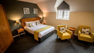 A bedroom with a large bed, two bedside tables, a small window, and two yellow armchairs.