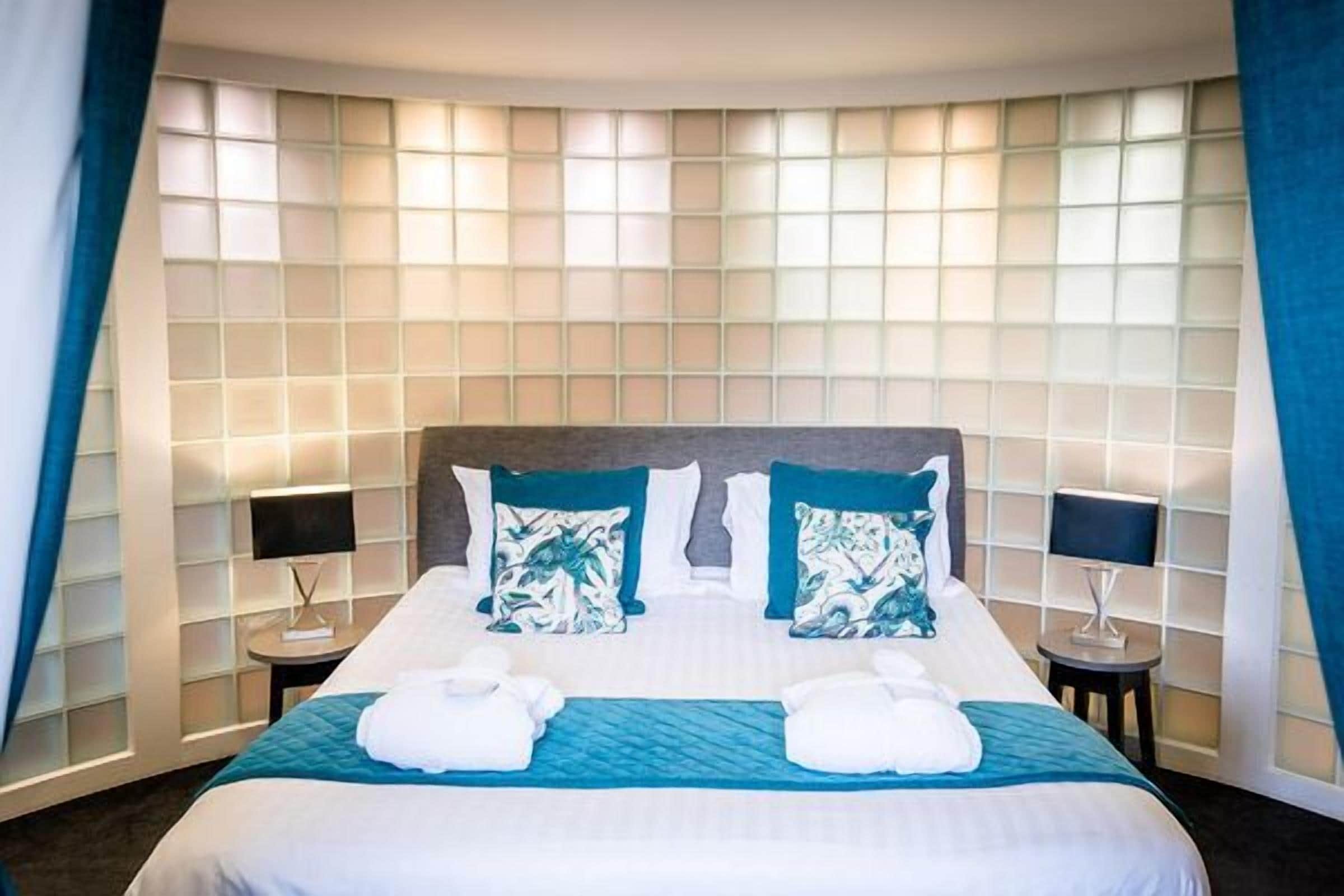 A hotel room with a large bed, two bedside tables, and a window with curtains.