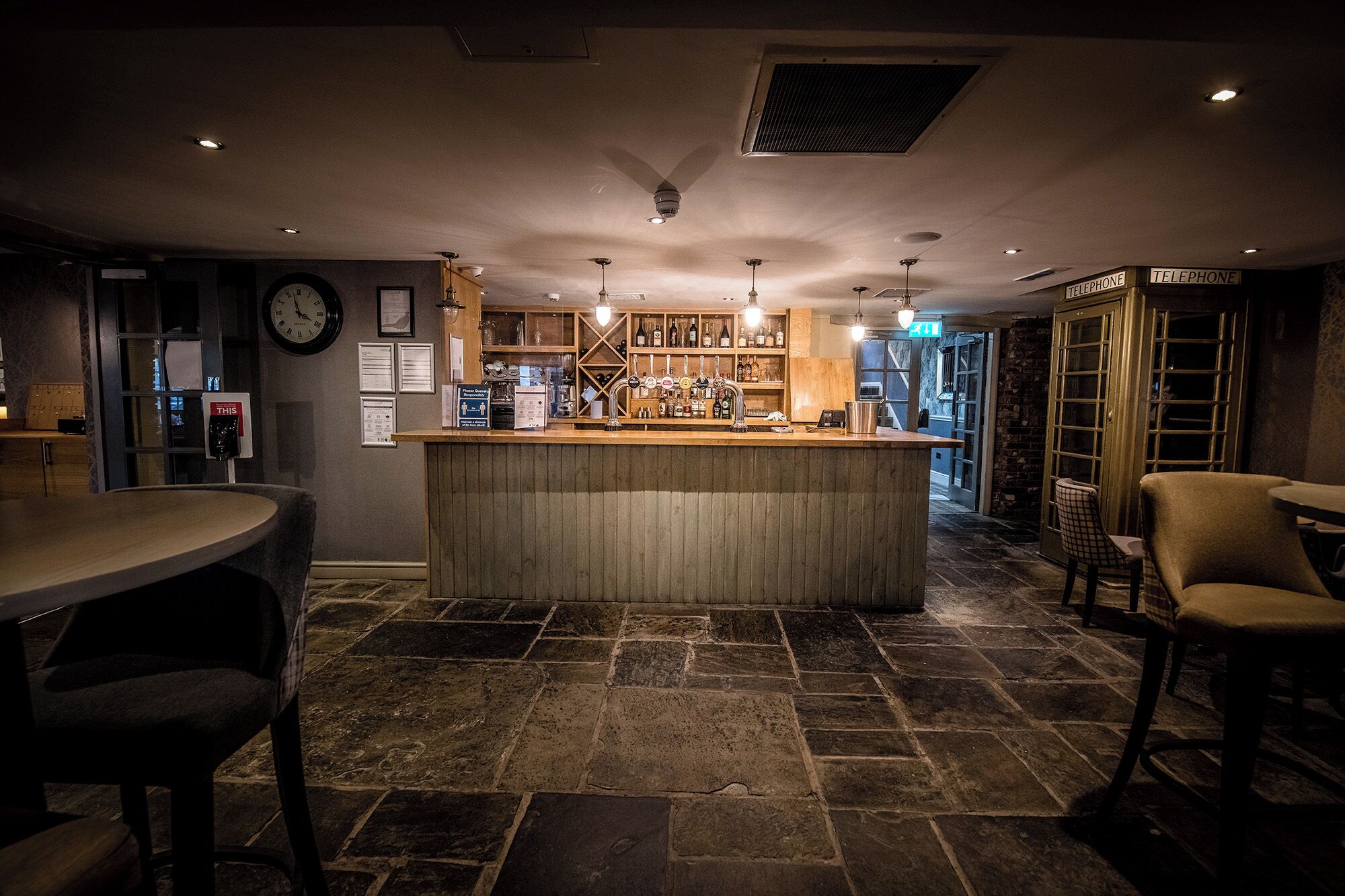 Een bar met een houten toonbank, stenen vloer en een klok aan de muur.