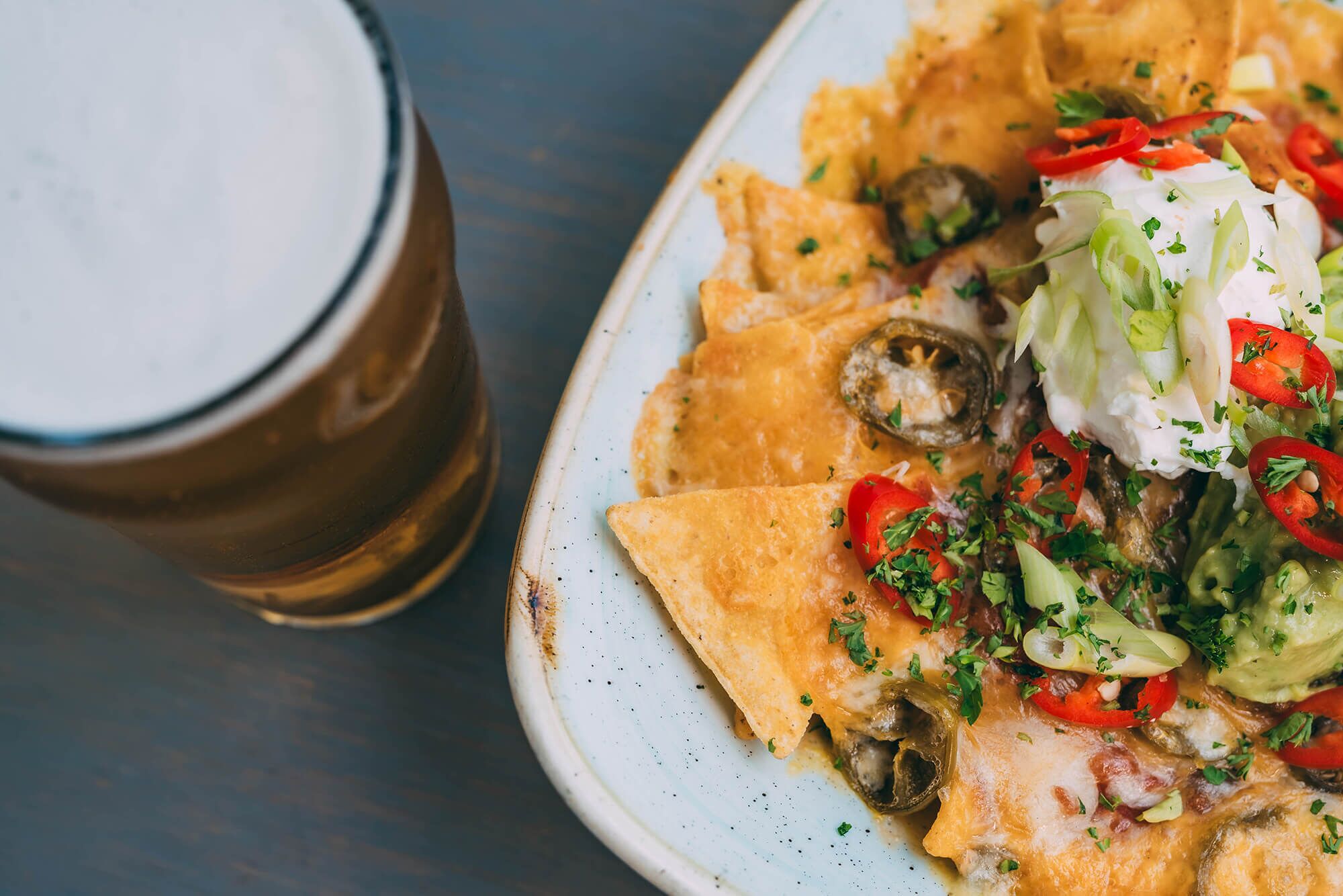 Nachos topped with cheese, jalapeños, and sour cream, served on a plate next to a glass of beer.