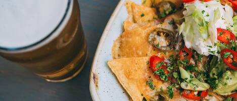 Nachos topped with cheese, jalapeños, and sour cream, served on a plate next to a glass of beer.