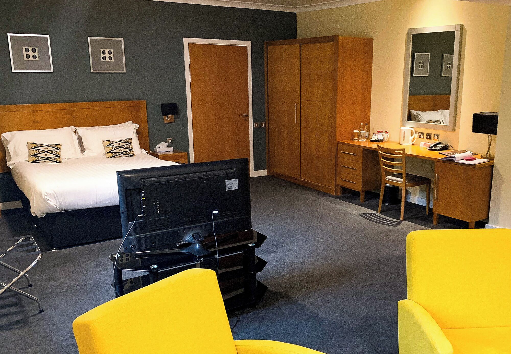 A hotel room with a bed, a desk, a chair, a wardrobe, and a television.