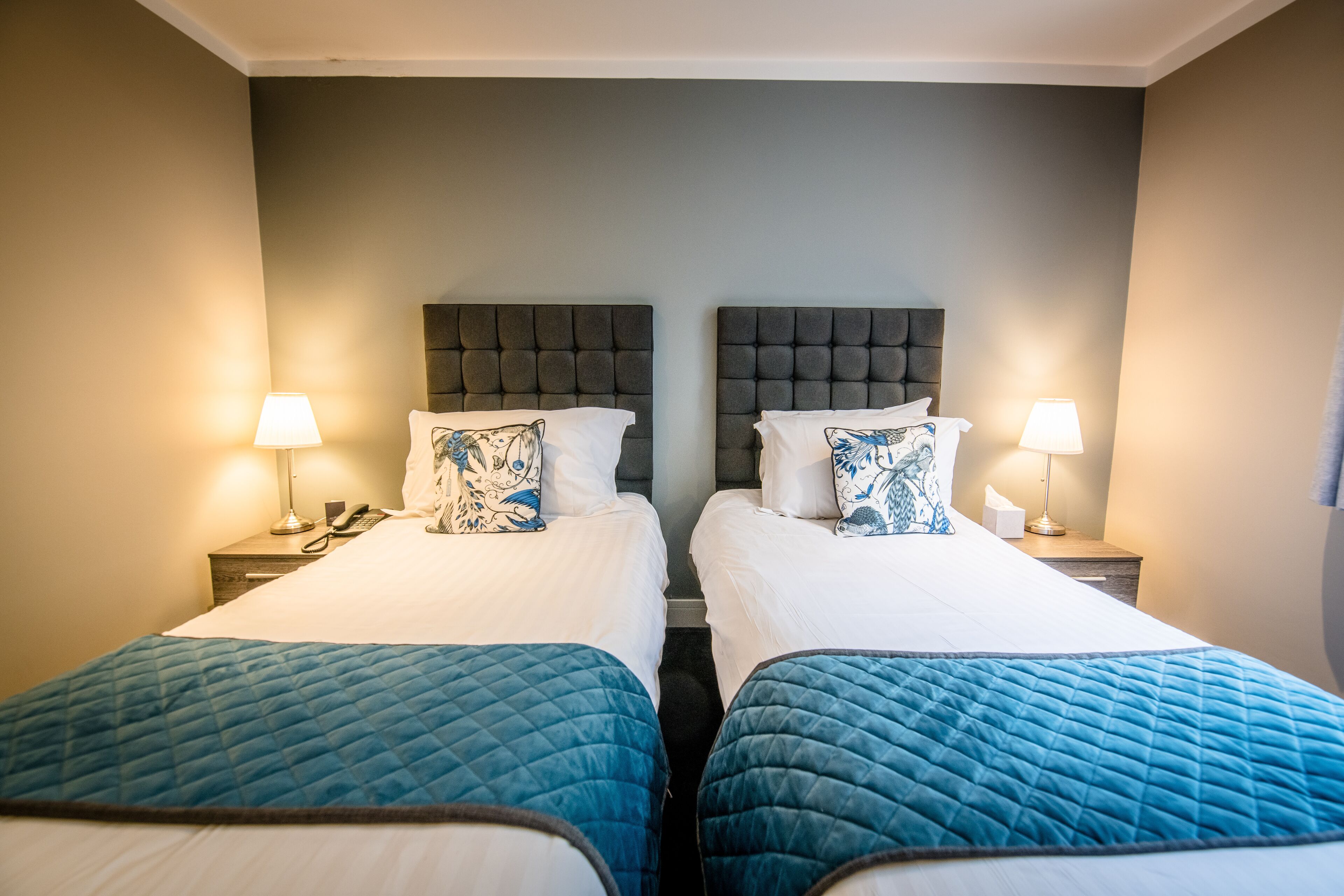 A hotel room with two beds, each with a headboard, a bedside table with a lamp, and a phone.