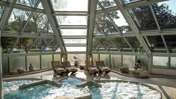 An indoor heated pool with wooden loungers and a glass ceiling.