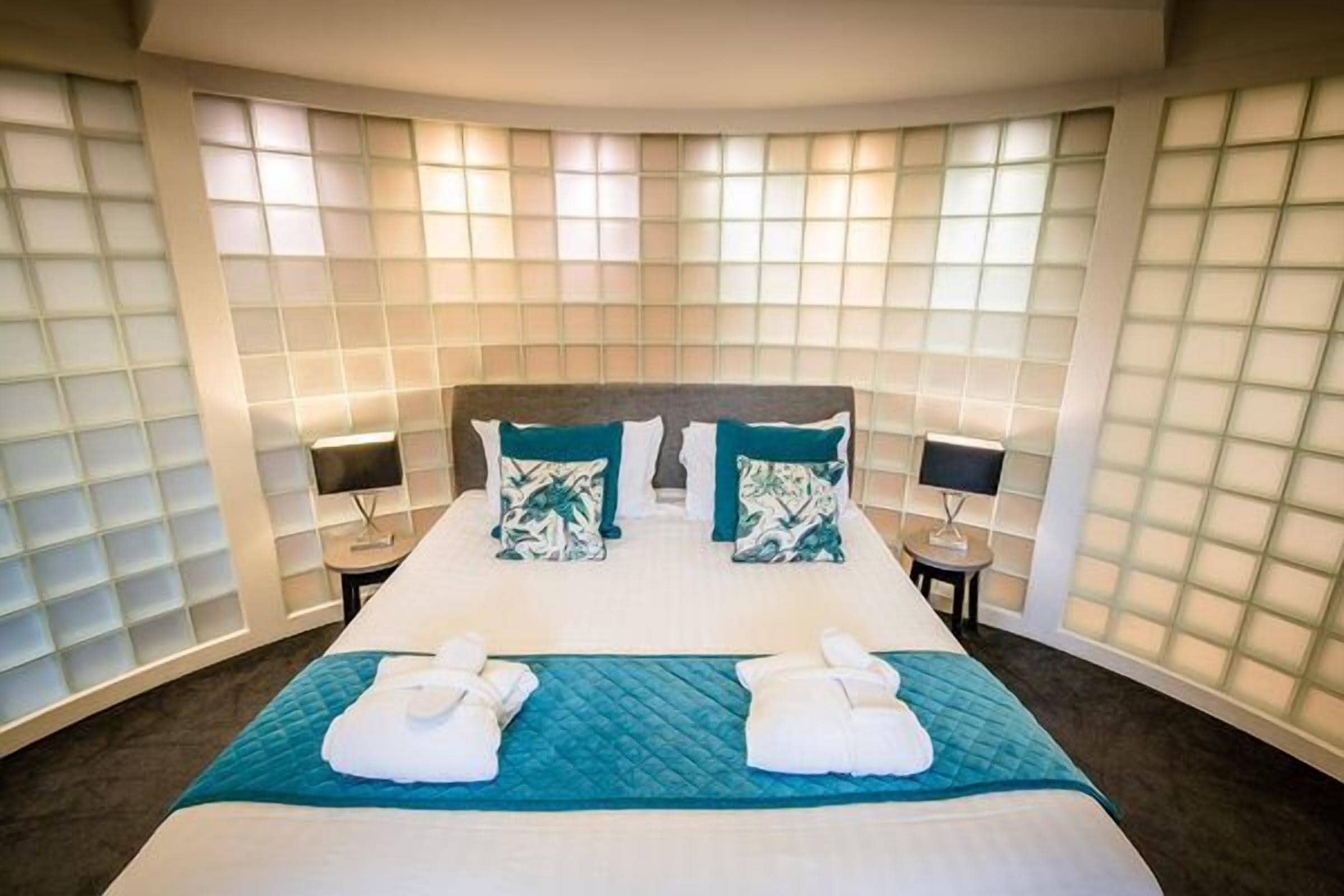 A hotel room with a large bed, two bedside tables, and a wall with a grid pattern.