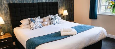 A neatly made bed with a dark headboard, white bedding, and a teal accent. There are two bedside lamps and a window with curtains.