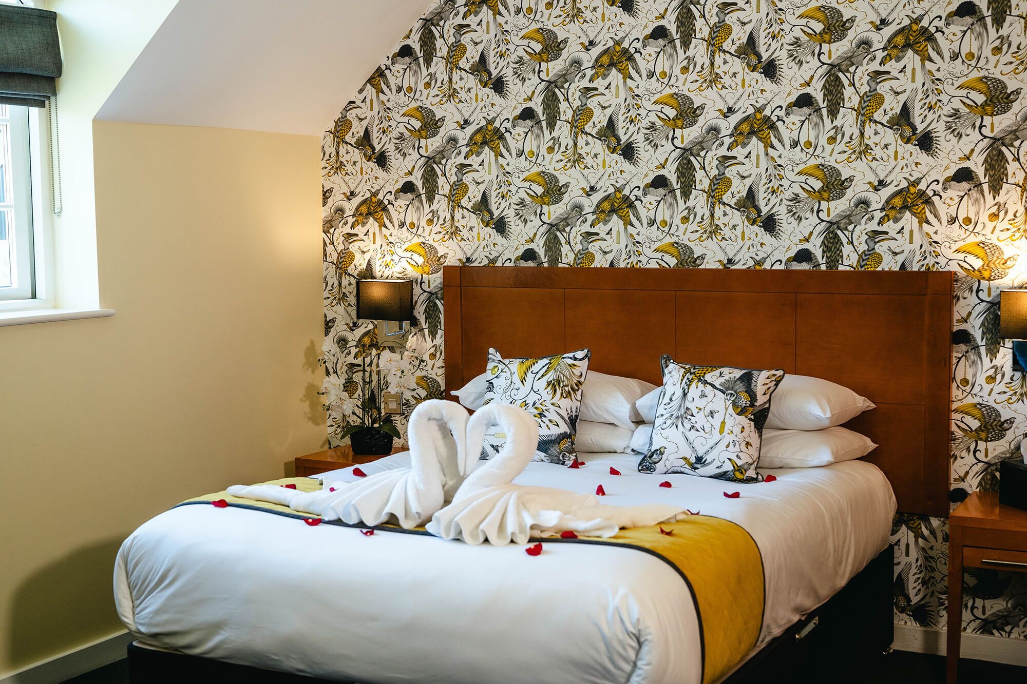 A hotel room with a large bed, a wooden headboard, and floral wallpaper.