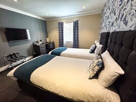 Habitación de hotel con dos camas, un escritorio, una silla, un televisor de pantalla plana y una ventana con cortinas.