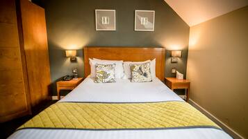 Quarto de hotel com uma cama grande, duas mesas de cabeceira com abajures e obras de arte na parede.