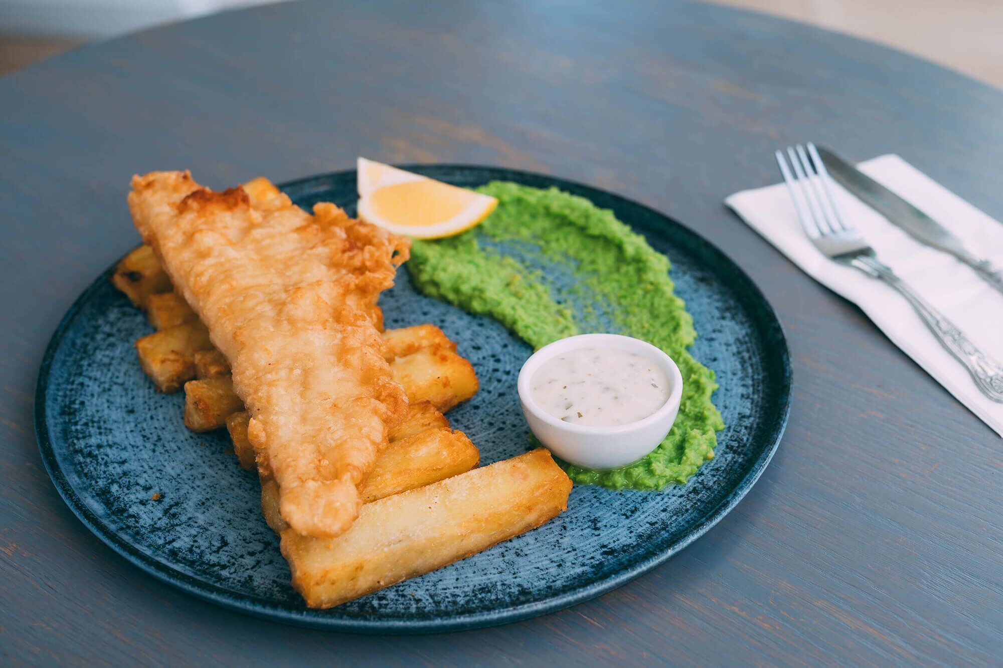 Um prato com peixe frito, batatas fritas, um ovo cozido e um molho verde.