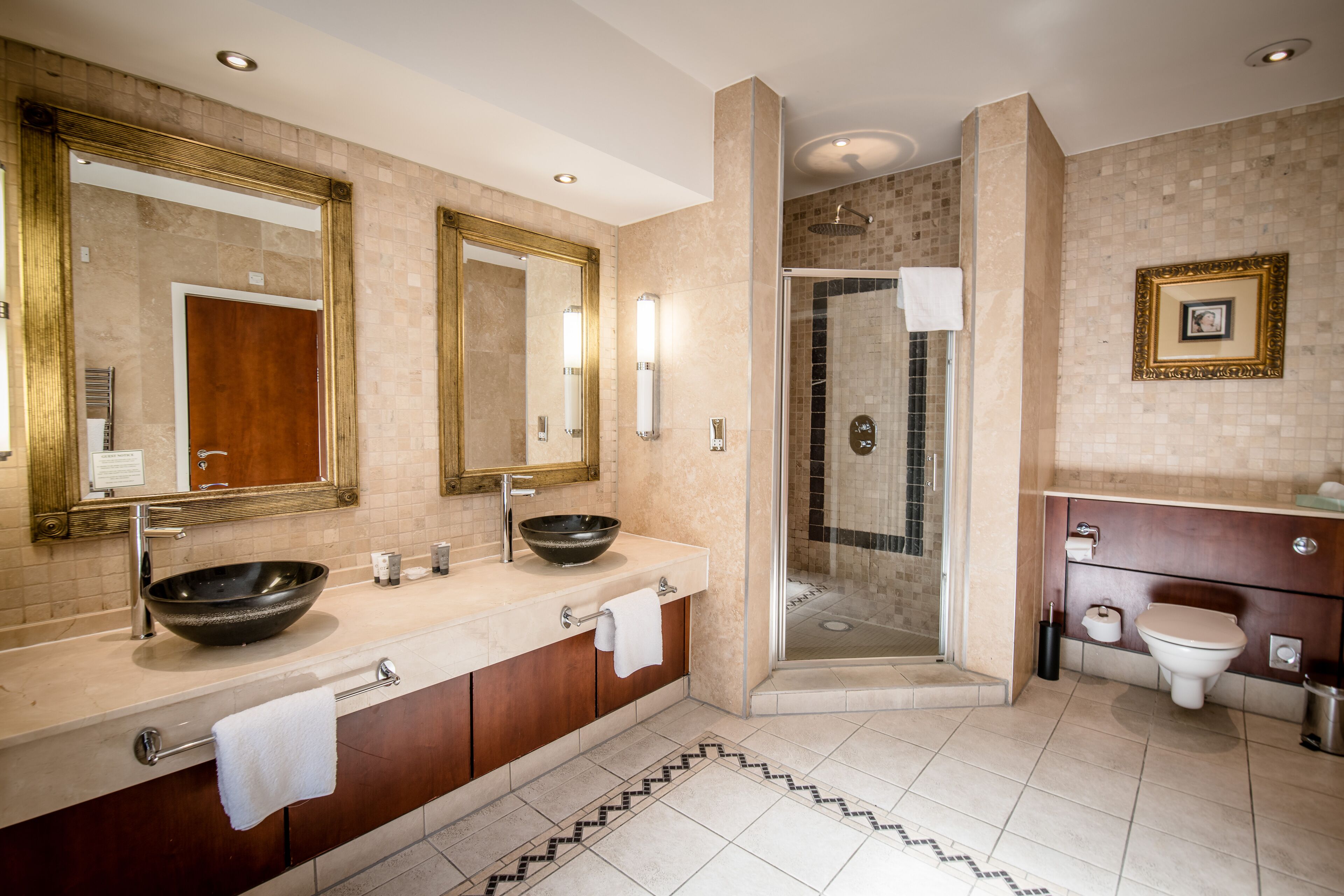 A modern bathroom with a large mirror, dual sinks, a glass-enclosed shower, and a toilet.