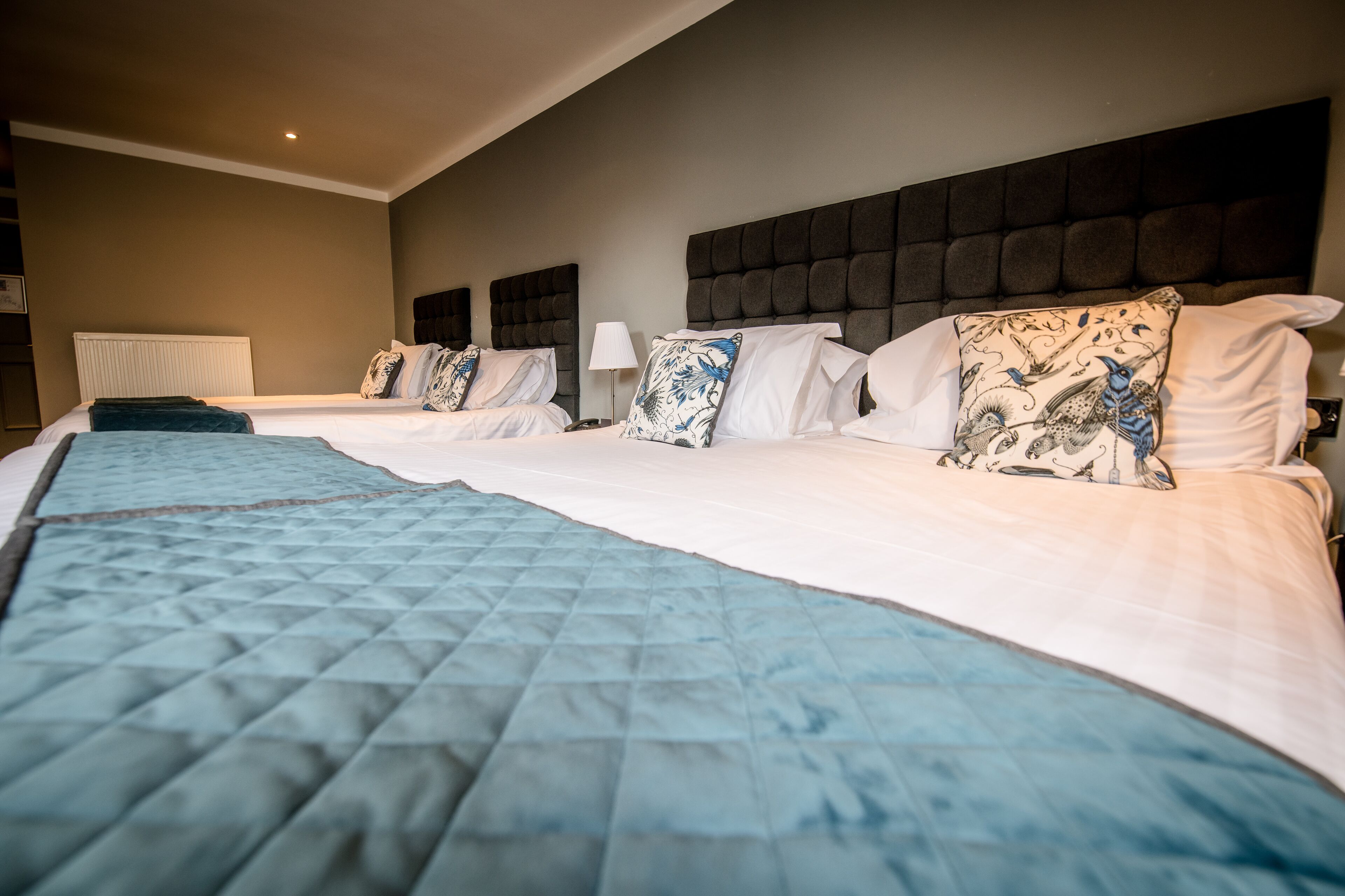 Habitación de hotel con dos camas, una colcha acolchada grande y un cabecero oscuro.