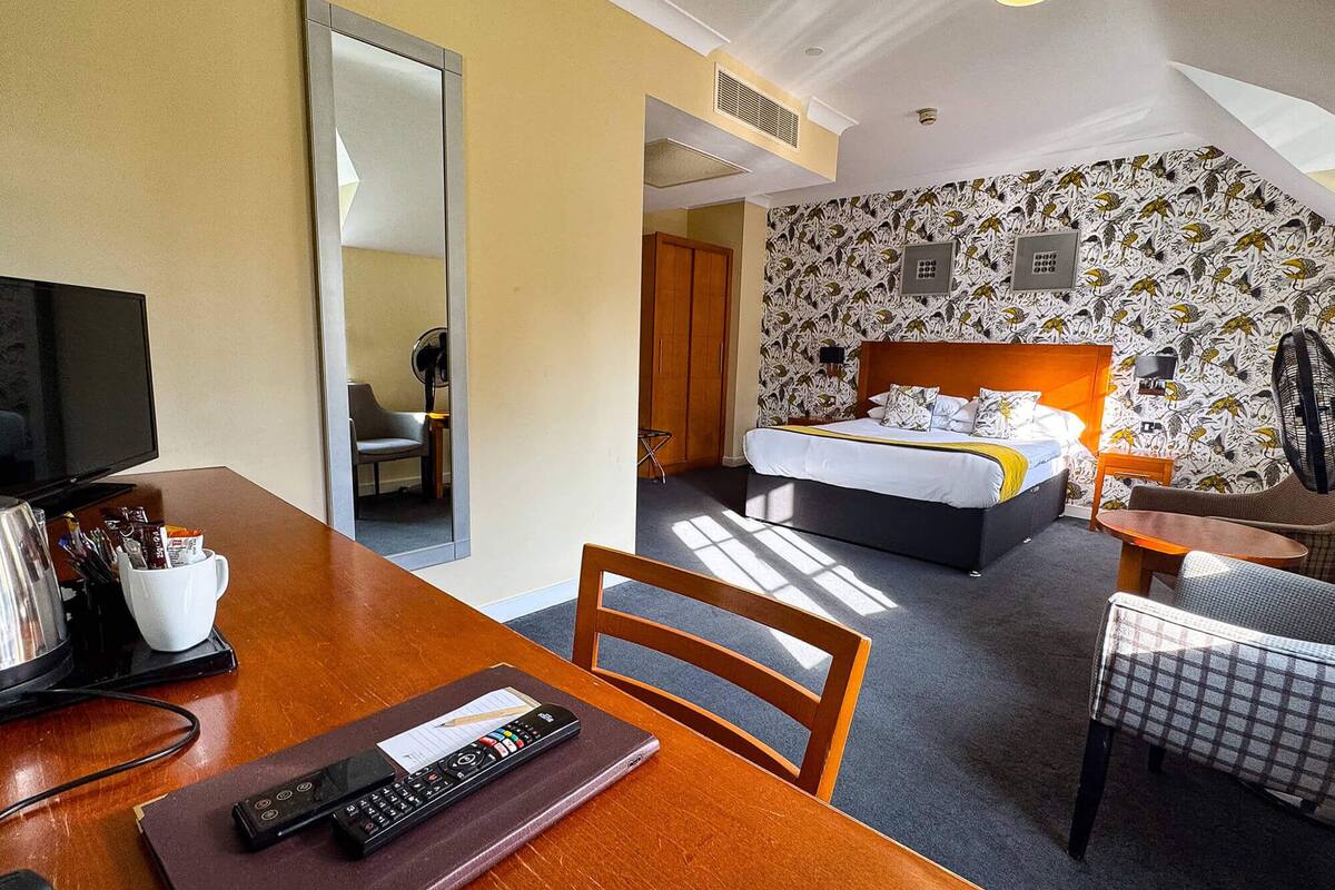 Habitación de hotel con cama, escritorio con televisor, silla, mesa y espejo.