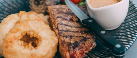 Un plato con bistec a la parrilla, aros de cebolla y una taza de salsa.