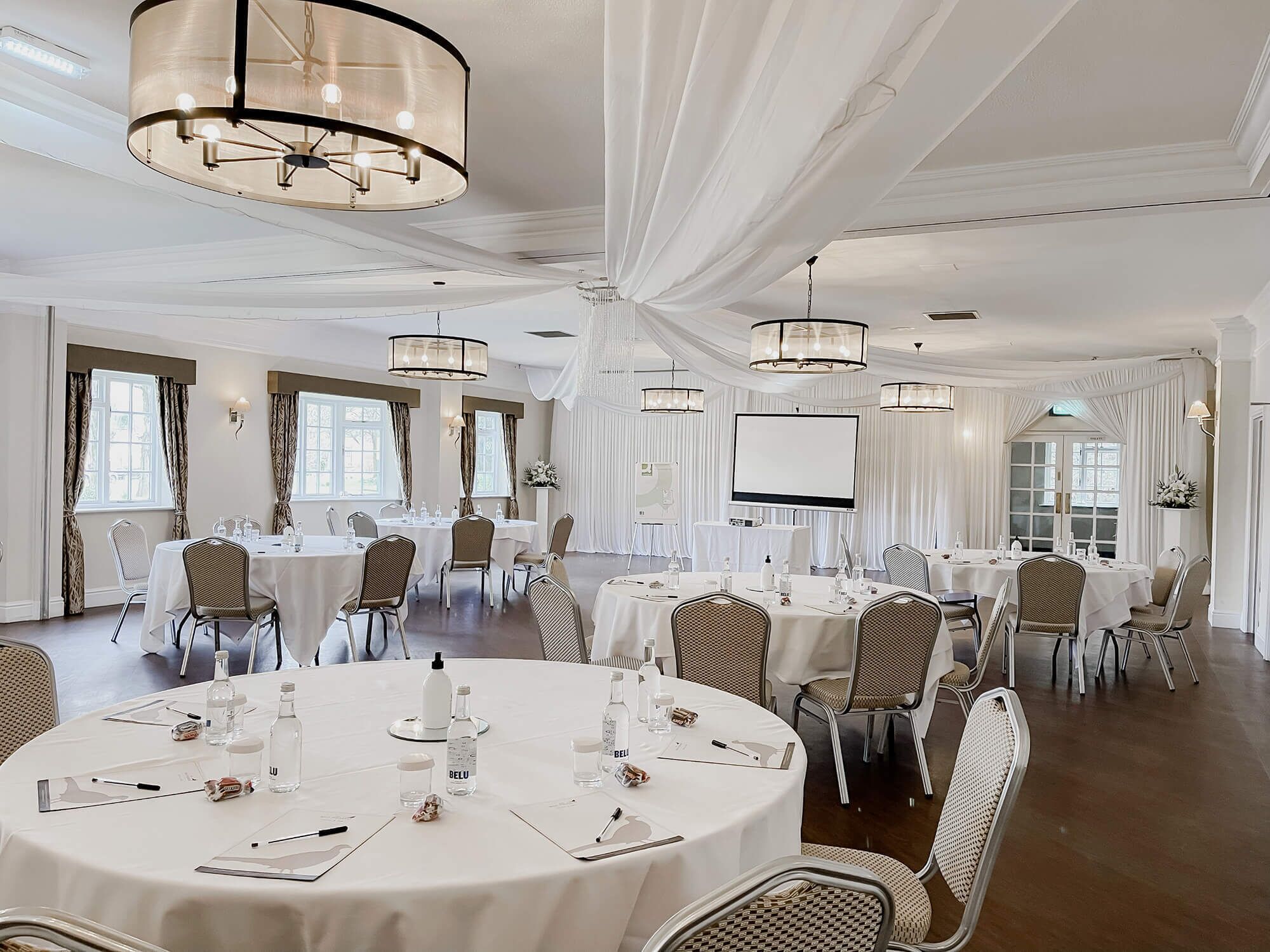 Un salón de conferencias con mesas redondas, cortinas blancas y candelabros.