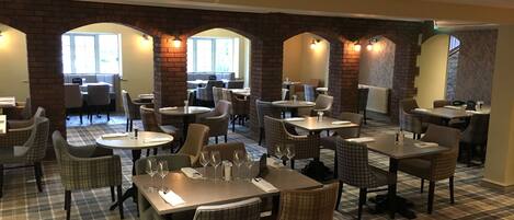 A restaurant with checkered flooring, brick arches, and multiple dining tables and chairs.