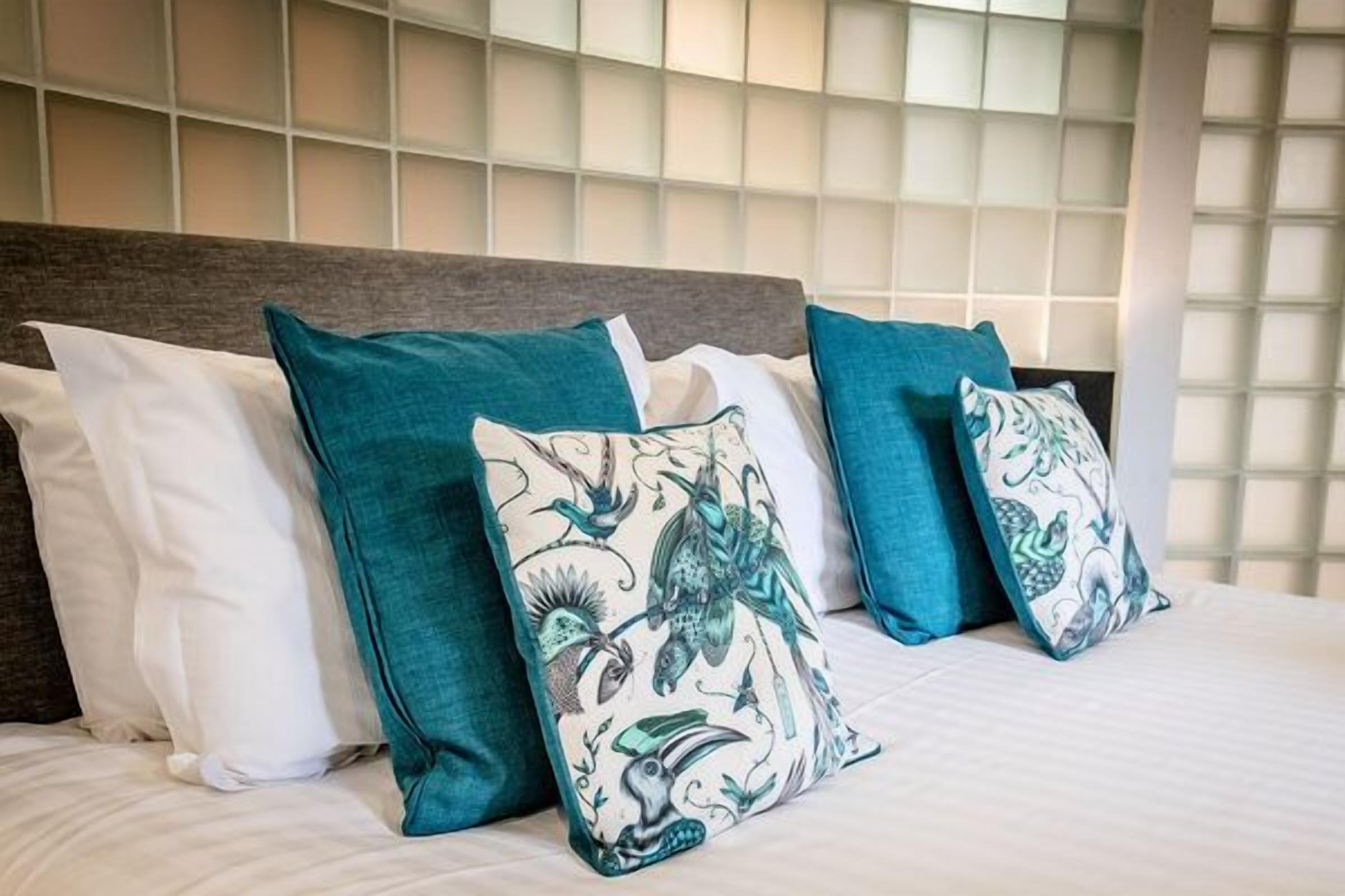Un lit avec des oreillers blancs et turquoise, une tête de lit en bois et une fenêtre à carreaux.