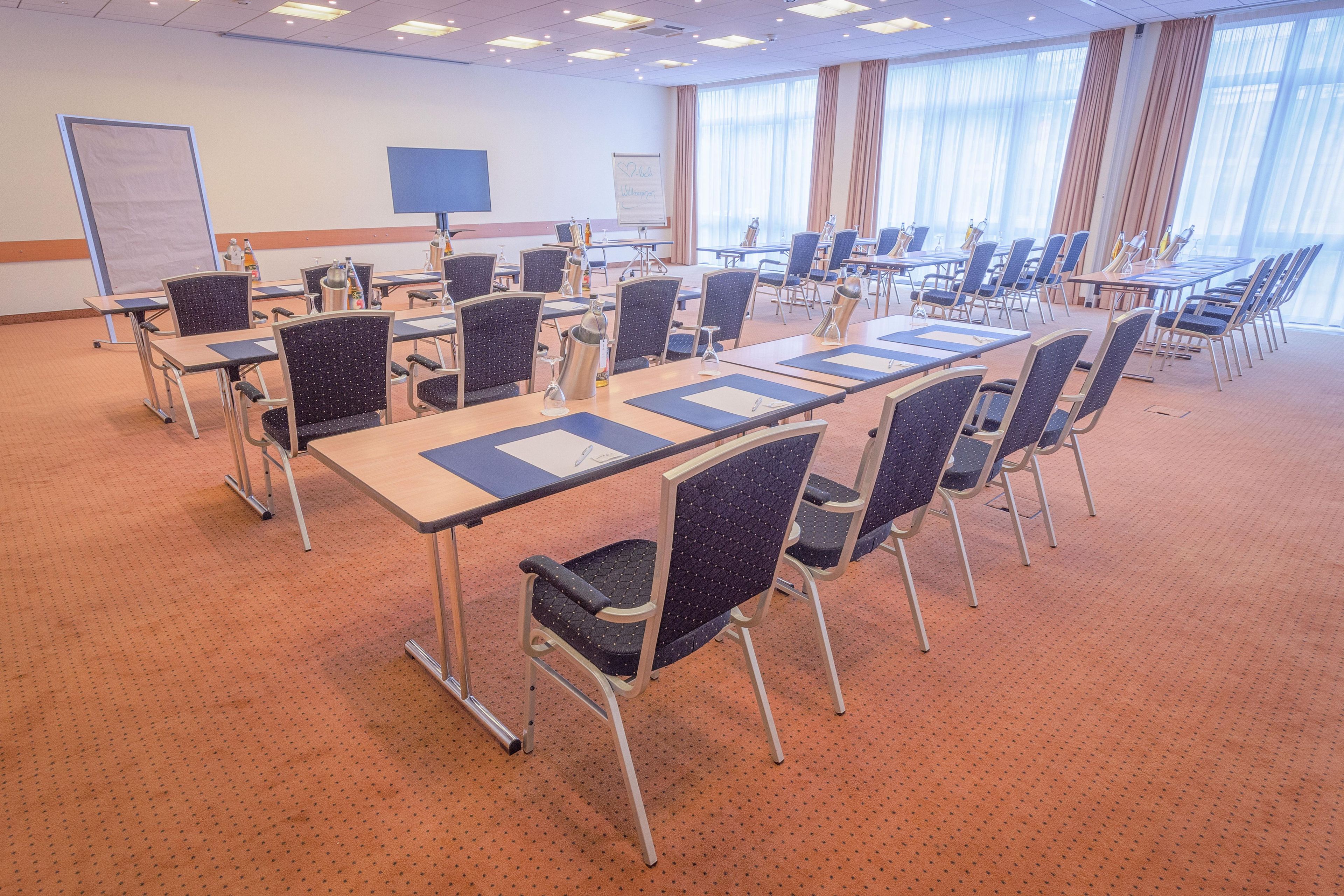 Un salón de conferencias con una larga mesa, sillas, una pizarra y una pantalla de proyector.