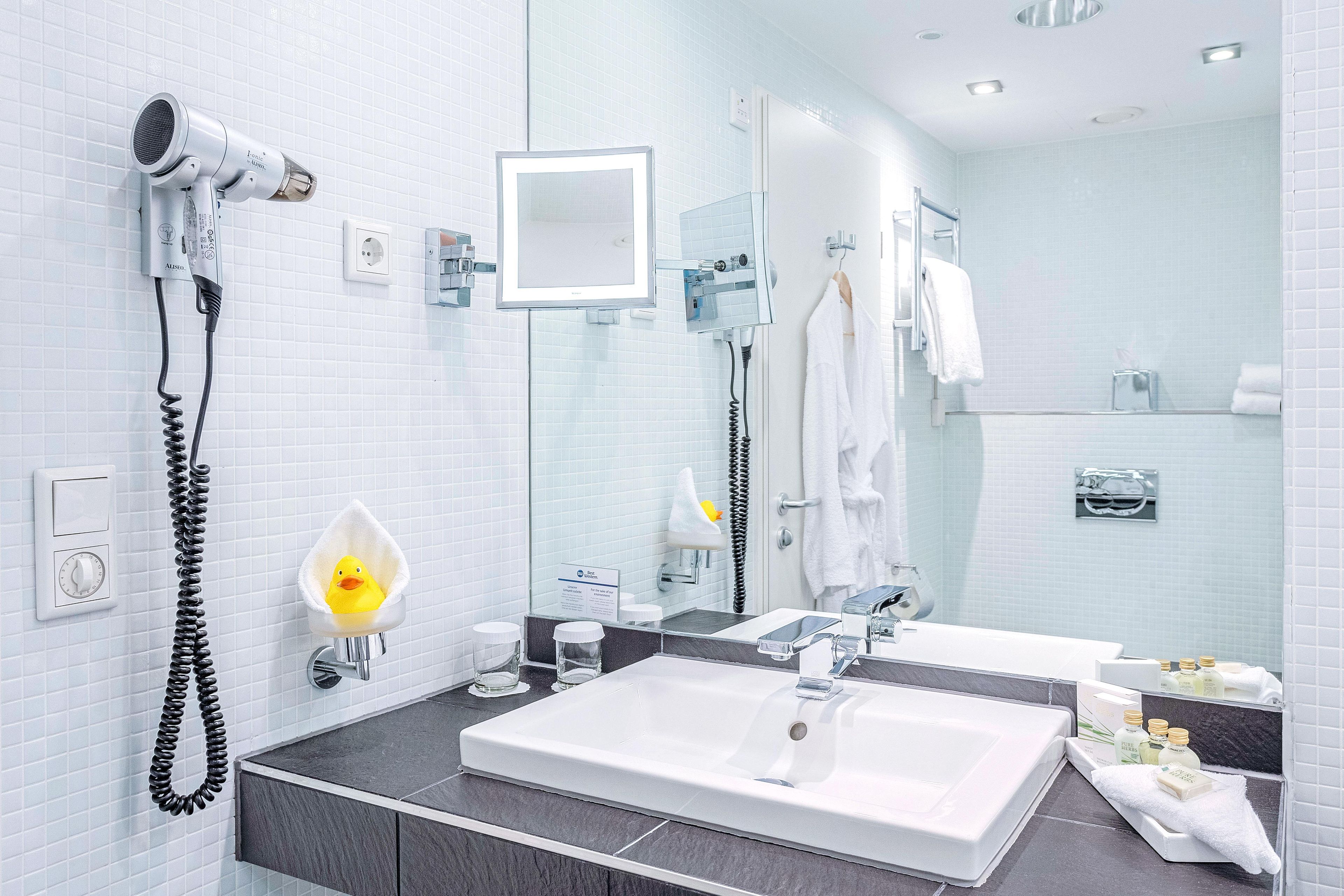 A modern bathroom with a large mirror, a sink, a hairdryer, and a towel rack.
