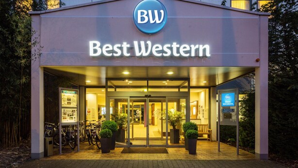 Entrada de un hotel con un cartel que dice 'Best Western', puerta de cristal y plantas en macetas.