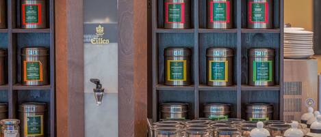 Mostrador de una cafetería con diversos productos de té y café, incluyendo latas y tazas de vidrio.