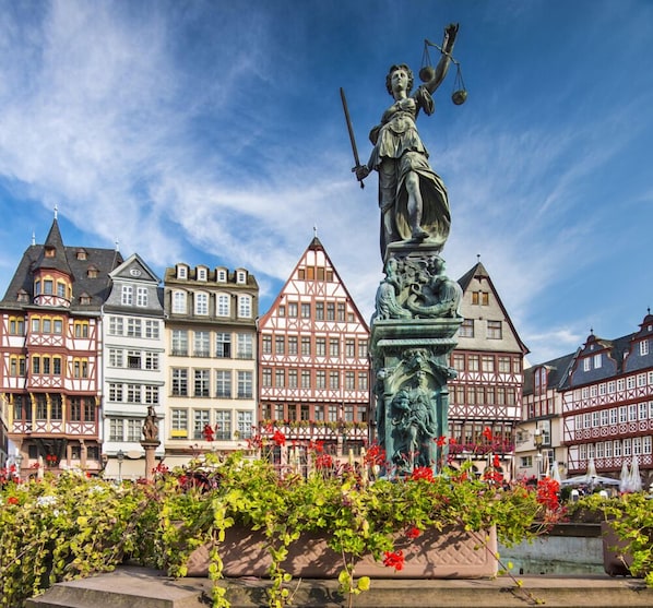 Eine Statue einer Frau, die Waage und Schwert hält, umgeben von farbenfrohen Fachwerkhäusern.