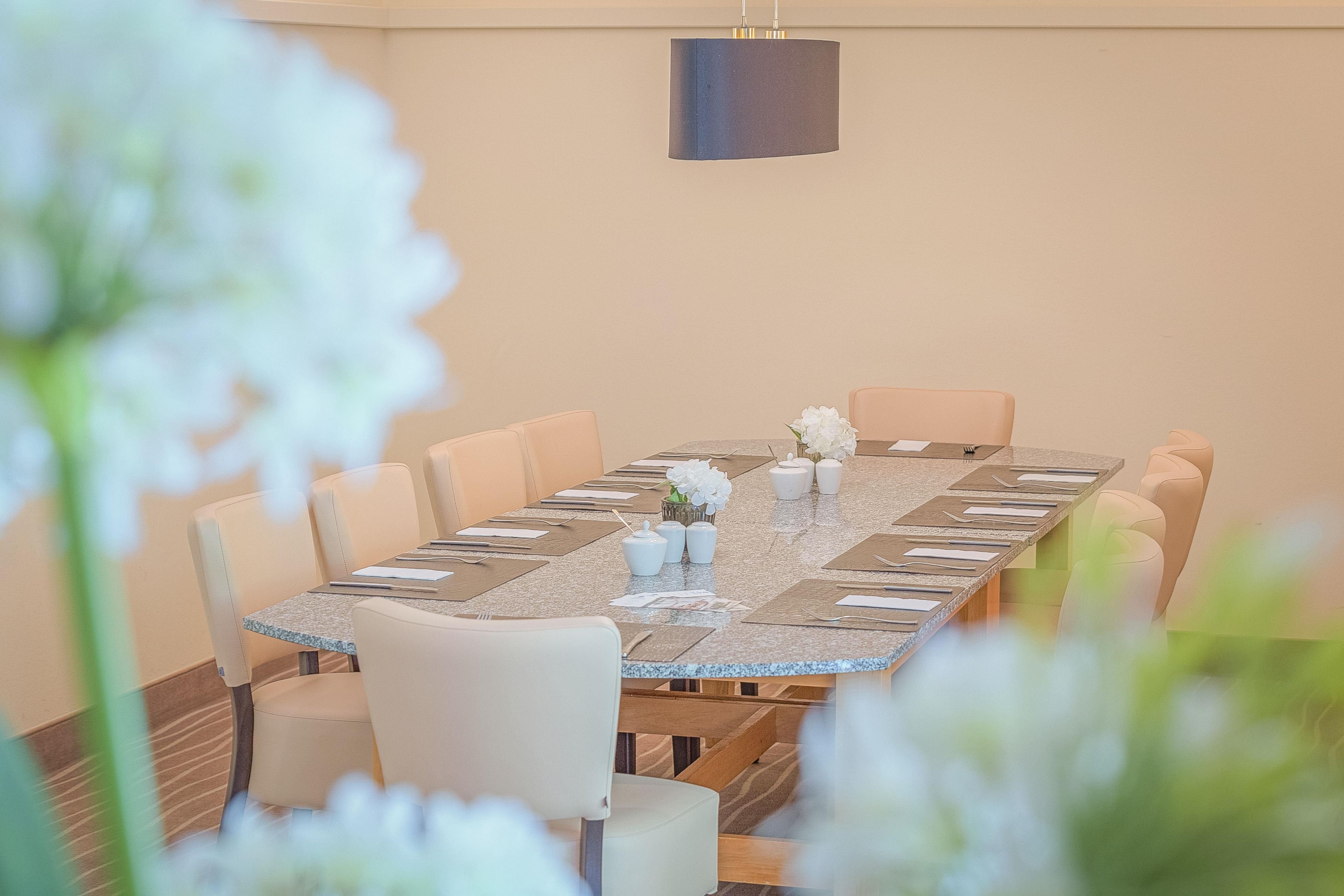A conference room with a long table set for a meeting, surrounded by chairs, with a simple chandelier above.