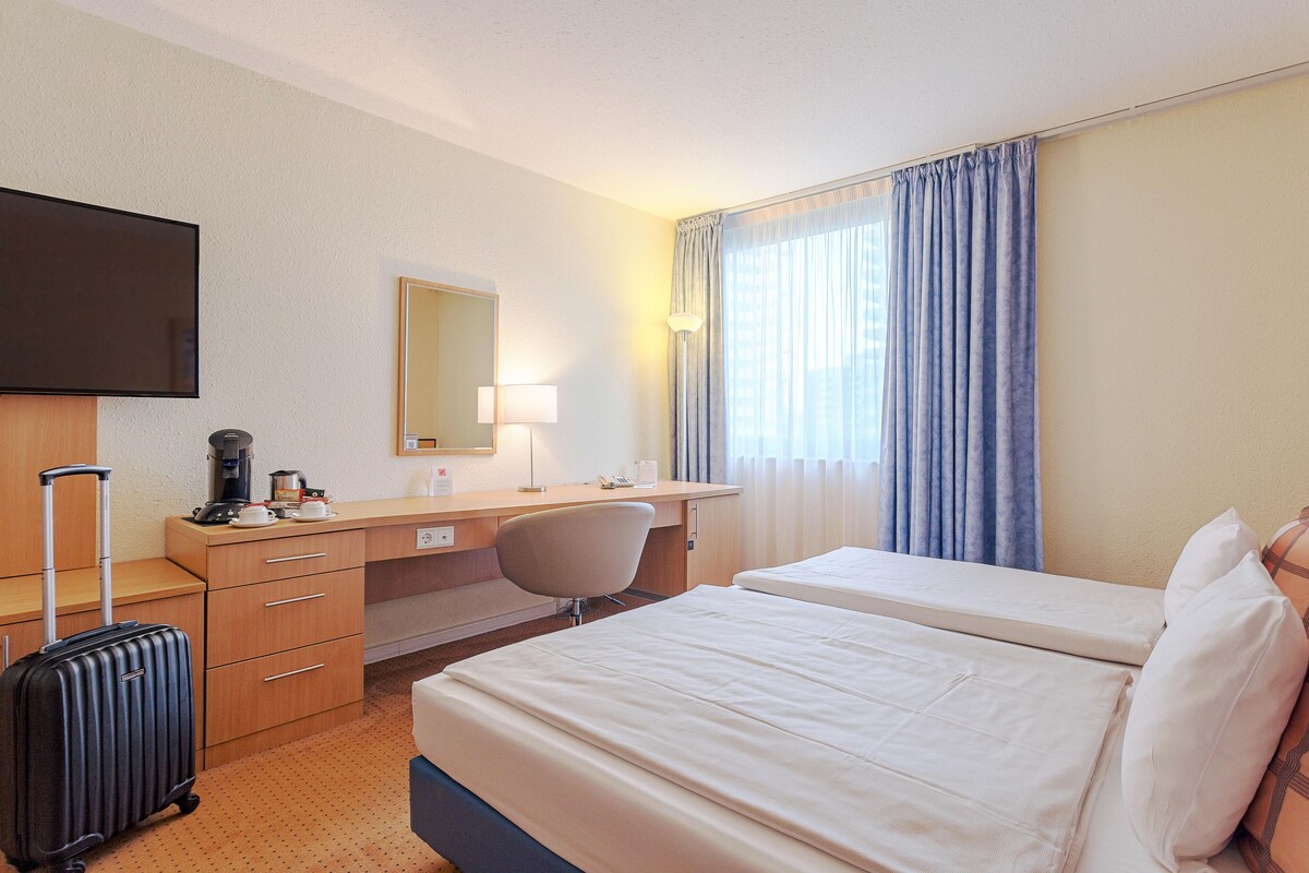 Ein Hotelzimmer mit Bett, Schreibtisch, Stuhl, Fernseher und Koffer.