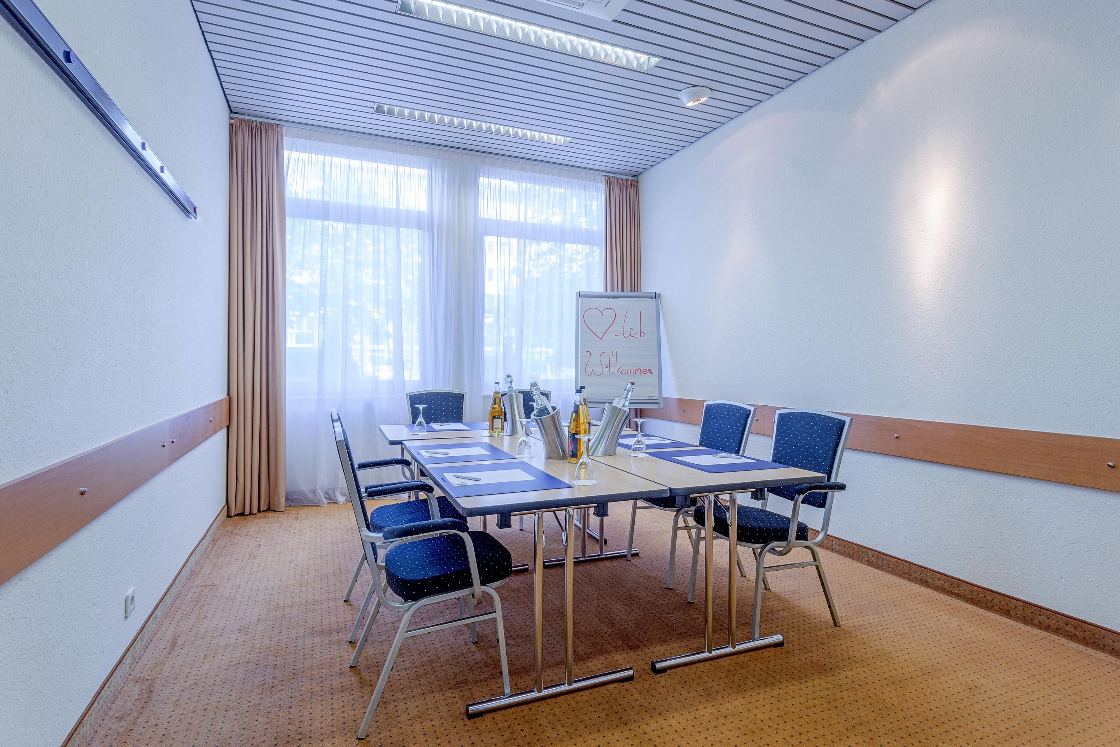 Une salle de conférence avec une longue table, des chaises, un tableau blanc et une fenêtre avec des rideaux.